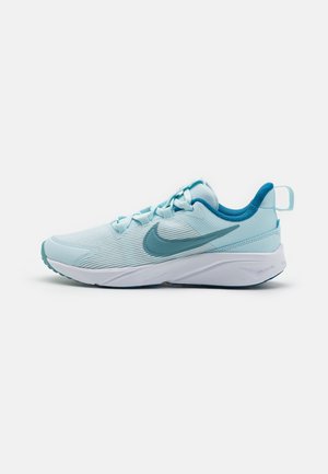 Zapatilla deportiva de color azul claro con parte superior texturizada, detalles en azul oscuro, suela acolchada y una entresuela blanca de contraste. Presenta un diseño con cordones.