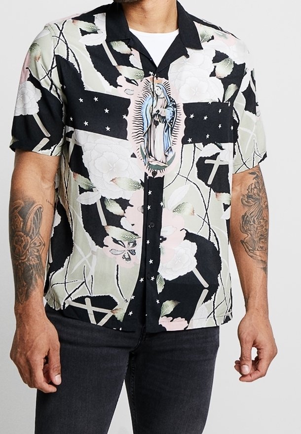Černá košile s krátkým rukávem s květinovými a křížovými vzory, která má uprostřed ilustraci postavy. Vyrobena z hladkého, lehkého materiálu.