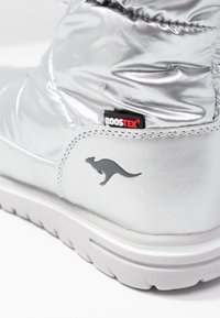 Stříbrná vycpaná bota s texturovanou bílou podrážkou, elastickým svrškem, štítkem s logem ROOSTEX a šedým emblémem klokana na boku.