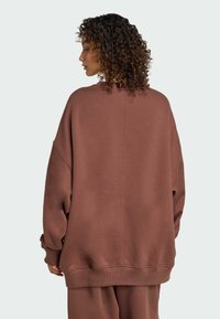 Oversized hnědá mikina z měkkého materiálu s kulatým výstřihem, spadlými rameny a žebrovanými manžetami a lemem. Hladký, texturovaný vzhled.