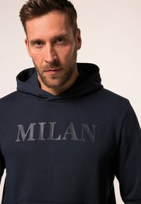 Felpa navy con una prominente stampa nera opaca "MILAN" sul davanti, realizzata in un morbido tessuto testurizzato, con cappuccio regolabile.