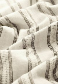 Tissu blanc doux avec des rayures horizontales noires et un motif de tissage texturé, montré en gros plan avec des plis doux.