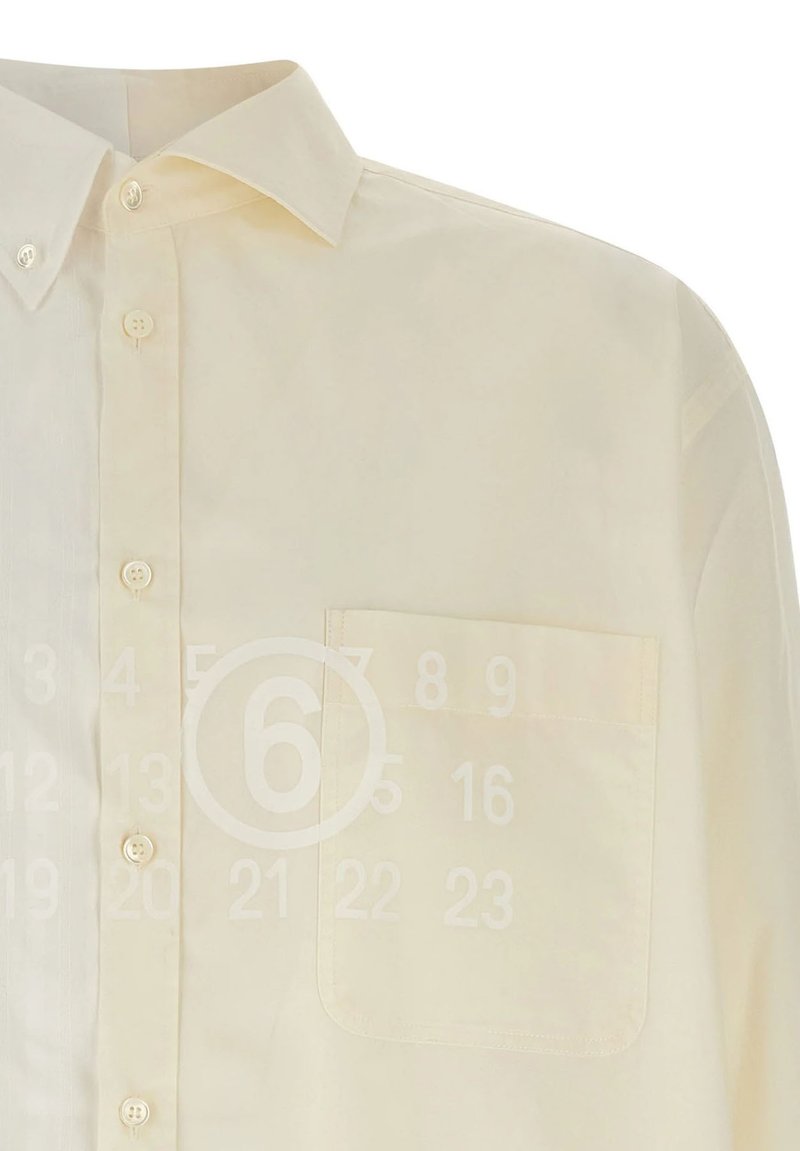 Camicia beige a maniche lunghe con bottoni, colletto a punta e taschino sul petto. I bottoni sono di colore chiaro e cuciti sulla patta frontale.