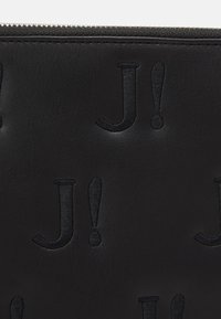 Czarna skórzana saszetka z wytłoczonym wzorem "J!" powtarzającym się w regularnym układzie. Charakteryzuje się gładką fakturą i srebrnym zamkiem błyskawicznym u góry.