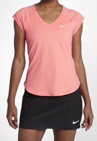 Top atlético de color rosa con escote en V y mangas cortas, combinado con una falda corta negra. Presenta el logo de Nike en blanco en ambas prendas. La tela parece suave y ligera.