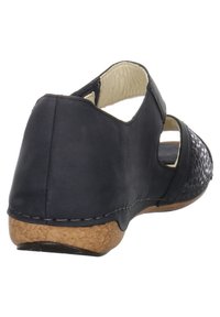 Sandale en cuir noir avec un panneau tissé texturé, arrière ouvert et semelle en liège. Présente des découpes rondes et des détails de couture le long du bord.