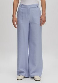 Lichtblauwe, wijde broek gemaakt van textuurstof, met een hoge taille en subtiele plooidetails, gecombineerd met schoenen in neutrale kleuren.