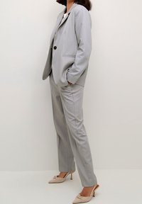 Costume ajusté gris clair avec une coupe slim, blazer à un bouton et pantalons à plis plats ; comprend des poches latérales et de fines rayures discrètes.