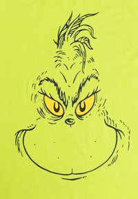 Maglietta verde con un'illustrazione in contorno nero del volto del Grinch, con occhi gialli, dettagli di pelliccia prominenti e un'espressione giocosa.