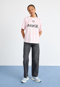 Rožinė ir balta juostelėta marškinė su juodu Nike logotipu; derinamos su pilkomis džinsomis ir šviesiai mėlynais sportiniais batais. Lygi medžiaga ir laisvas kirpimas.