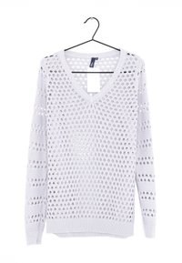 Pull en V gris clair en tissu tricoté, présentant un motif à trous ouverts et des poignets et un ourlet côtelés. Suspendu à un crochet noir.