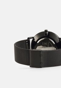 Montre avec bracelet en maille noire, dotée d'un boîtier noir brillant et d'un cadran rond. Comprend un fermoir rabattable sécurisé et un design résistant à l'eau.