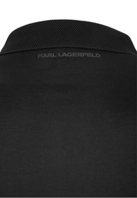 Schwarzes Poloshirt mit strukturiertem Kragen, auf dem hinten in dunkler Schrift "KARL LAGERFELD" geprägt ist. Glatte Stoffoberfläche.