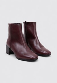 Bottines en cuir bordeaux avec un bout carré et un talon bloc moyen, dotées d'une fermeture éclair sur le côté pour un enfilage facile. Texture lisse et design épuré.