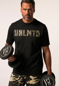 Camiseta negra con "UNLMTD" en letras de camuflaje, combinada con pantalones cortos de camuflaje. Sosteniendo dos mancuernas negras con un logo.