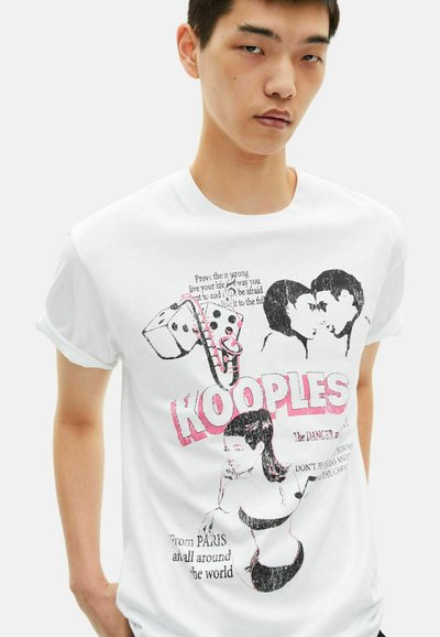 White cotton t-shirt featuring black and pink graphic prints, including text and illustrations of dice and a figure, round neckline and rolled sleeves.