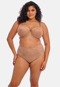 Beha en hoog-getailleerde slipset in zacht beige stof, met vetersluiting op de slip en een decoratieve strik aan de voorkant van de beha.