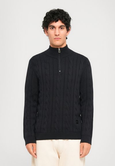 Mørk marineblå kabelstrikket sweater med høj krave og halvlange lynlås. Har ribbet kant og manchetter, lavet af blødt, tekstureret stof.