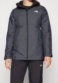 Mörkgrå isolerad jacka med en texturerad yta, dragkedjeslutning, justerbar huva, två framfickor och logotyp på bröstet och ärmen.