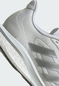 Weißer Sportschuh mit strukturiertem Mesh-Obermaterial, Gummisohle und grauen Akzenten. Verfügt über ein schlankes Design und einen gepolsterten Kragen.