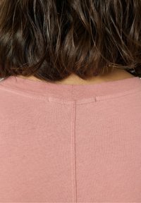 Różowy top z krótkim rękawem, z okrągłym dekoltem i miękką, fakturowaną tkaniną. Widoczne przeszycia na plecach dodają detali.