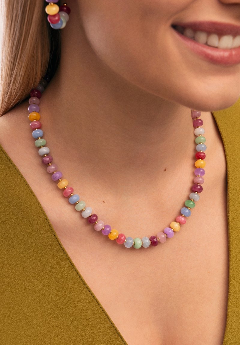Kralenketting met meerkleurige ronde stenen in pastelkleuren, afgewerkt met gouden accenten, gedragen met een groene top. De oorbellen passen bij de ketting.