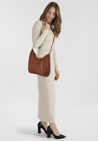 Borsa a spalla in pelle intrecciata marrone con superficie texture, dotata di una sola tracolla regolabile e hardware in tono oro, appoggiata su uno sfondo chiaro.