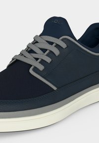 Baskets bleu marine avec lacets gris, bout en mesh texturé, panneaux latéraux en cuir et semelle en caoutchouc blanche.