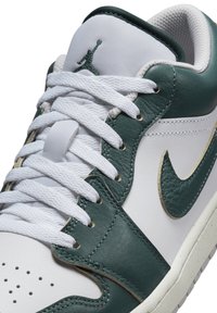 Vita lädersneakers med mörkgröna läderdetaljer, perforerad tå, gulddetaljer och vita snören. Jordan-logotypen på tungan.