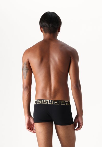 Black boxer shorts with a gold Greek key pattern on the waistband, made of smooth fabric, shown from the back against a white background.