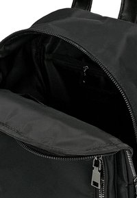 Interno di uno zaino in tessuto nero che presenta un compartimento principale e una piccola tasca con zip. Texture liscia con una chiusura a zip sicura.