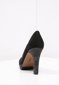 Black suede high heel shoe with a pointed toe and textured patterned heel. Leather insole visible, featuring the brand name.