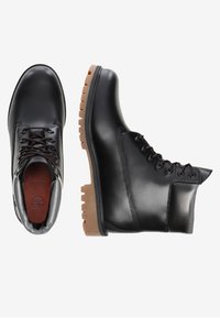 Botas de cuero negro con puntera redonda, diseño de cordones marrón y suela de goma con profundas tracciones. Textura suave, construcción robusta.