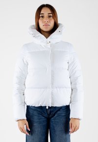Giacca a vento bianca con colletto alto, caratterizzata da una finitura lucida, bottoni a scatto e un design corto. Abbinata a jeans in denim scuro.
