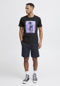Camiseta de algodón negra con un gráfico de palmera púrpura, combinada con pantalones cortos navy y zapatillas de caña alta negras. Diseño simple y casual.