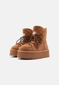 Καφέ σουέτ μποτάκια στον αστράγαλο με κομψές ραφές, παχιές σόλες από καουτσούκ και κλείσιμο με κορδόνια με μεταλλικές οπές και λογότυπο.