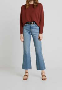 Pull côtelé couleur rouille, jean évasé taille haute bleu clair, et sandales à talons carrés imprimé léopard.