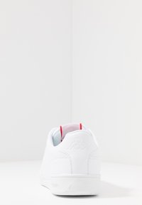 Weißer Sneaker mit glattem synthetischen Obermaterial, runder Zehenpartie und gepolsterter Kante. Verfügt über einen roten Akzent an der Ferse und Logo-Details an der Rückseite.