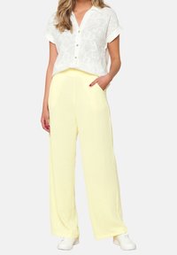 Biała haftowana bluzka z kołnierzykiem, zestawiona z żółtymi spodniami o szerokich nogawkach z teksturowanej tkaniny. Białe sneakersy dopełniają całość.