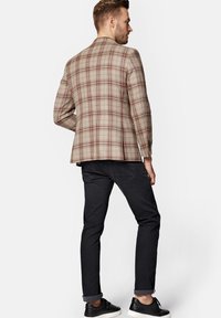 Beżowa marynarka w kratę w odcieniach czerwieni i brązu, zestawiona z ciemnymi dżinsami i czarnymi sneakersami. Marynarka posiada przeszycia na ramionach oraz detale guzików.