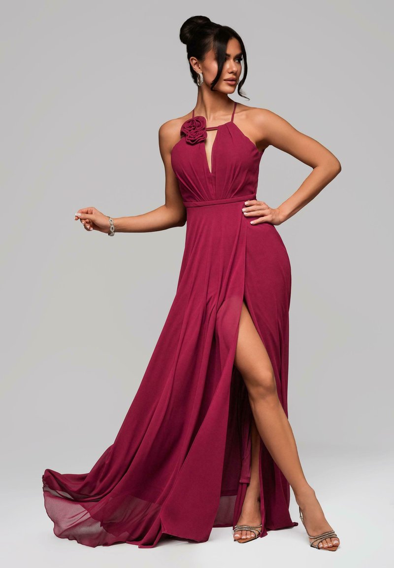 Abito halter bordeaux con un accento floreale, profondo scollo a V e spacco alta coscia. Realizzato in tessuto leggero con una gonna fluida. Tacchi argento.