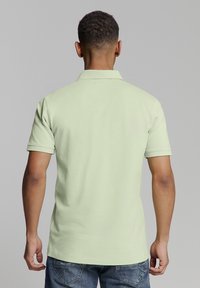 Lichtgroen poloshirt met een kraag, korte mouwen en een egale structuur. De achterkant heeft een schoon ontwerp en een getailleerde pasvorm.
