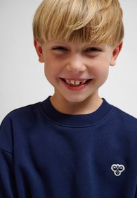 Marinblå sweatshirt med rund halsringning och ribbad ärm, med en liten broderad ljus design på vänster bröstområde.