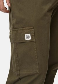 Olivegrüne Cargo-Hosen aus strapazierfähigem Stoff, mit einer aufgenähten Tasche am Oberschenkel und einem beschrifteten Logo-Tag. Glatte, matte Oberfläche.