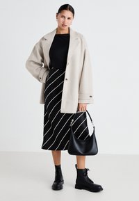 Beige oversized frakk, svart topp, svart-hvit stripete midi skjørt, svarte lærsoldatstøvler, og en svart håndveske.