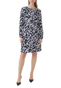 Marineblaues Kleid mit abstrakten schwarz-weißen und blauen Mustern, langen Ärmeln, rundem Ausschnitt und gerafftem Detail an der Taille, kombiniert mit schwarzen High Heels.