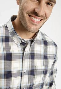 Koszula w kratę z guzikami w kolorze granatowym, białym i jasnoszarym. Posiada kieszeń na piersi oraz miękką, fakturowaną tkaninę.