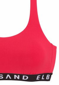 Reggiseno sportivo rosso in tessuto liscio. Presenta un'ampia fascia nera con testo bianco nella parte inferiore. Design semplice con scollatura rotonda.