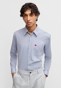 Camicetta azzurro chiaro con maniche lunghe, taschino sul petto e piccolo logo del marchio rosso. Realizzata in un tessuto liscio, i dettagli includono bottoni bianchi.