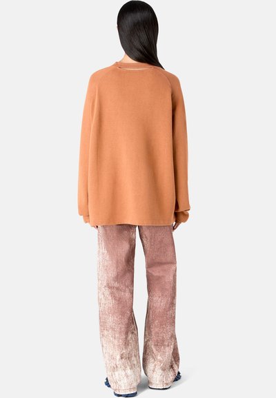 Rust-colored oversized fleece sweatshirt paired with high-waisted, light pink, textured flared pants. Simple design, soft fabric, relaxed fit.